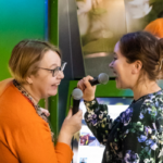 Kaksi naista laulaa mikrofoneihin selkä katsojaan päin. Taustalla suuri peili, josta naiset näkyvät.