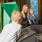 Kaksi naista ja kolme lasta tutkivat tiedekeskusnäyttelyn kohteita.