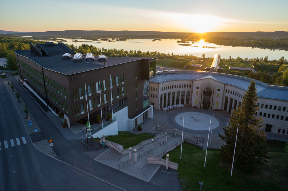 Keskikesällä keskiyön auringossa puurakenteinen Pilke-talo ja Arktikum-rakennus Ounasjoen rannalla.