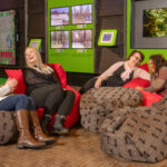 Neljä nauravaa naista istuu säkkituoleilla tiedekeskusnäyttelyssä. Taustalla metsäaiheisia tiedekeskuskohteita.